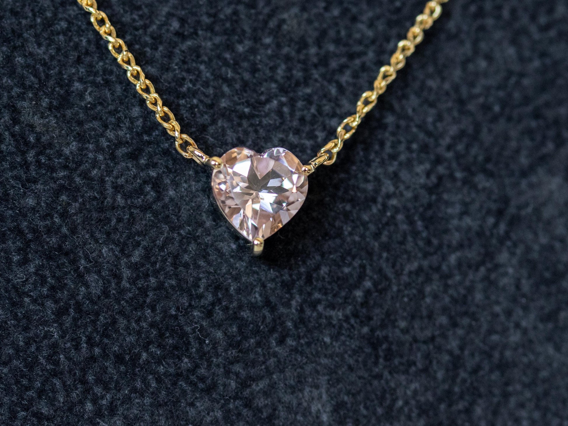 Heart-shaped diamond pendant on a gold chain against a dark background