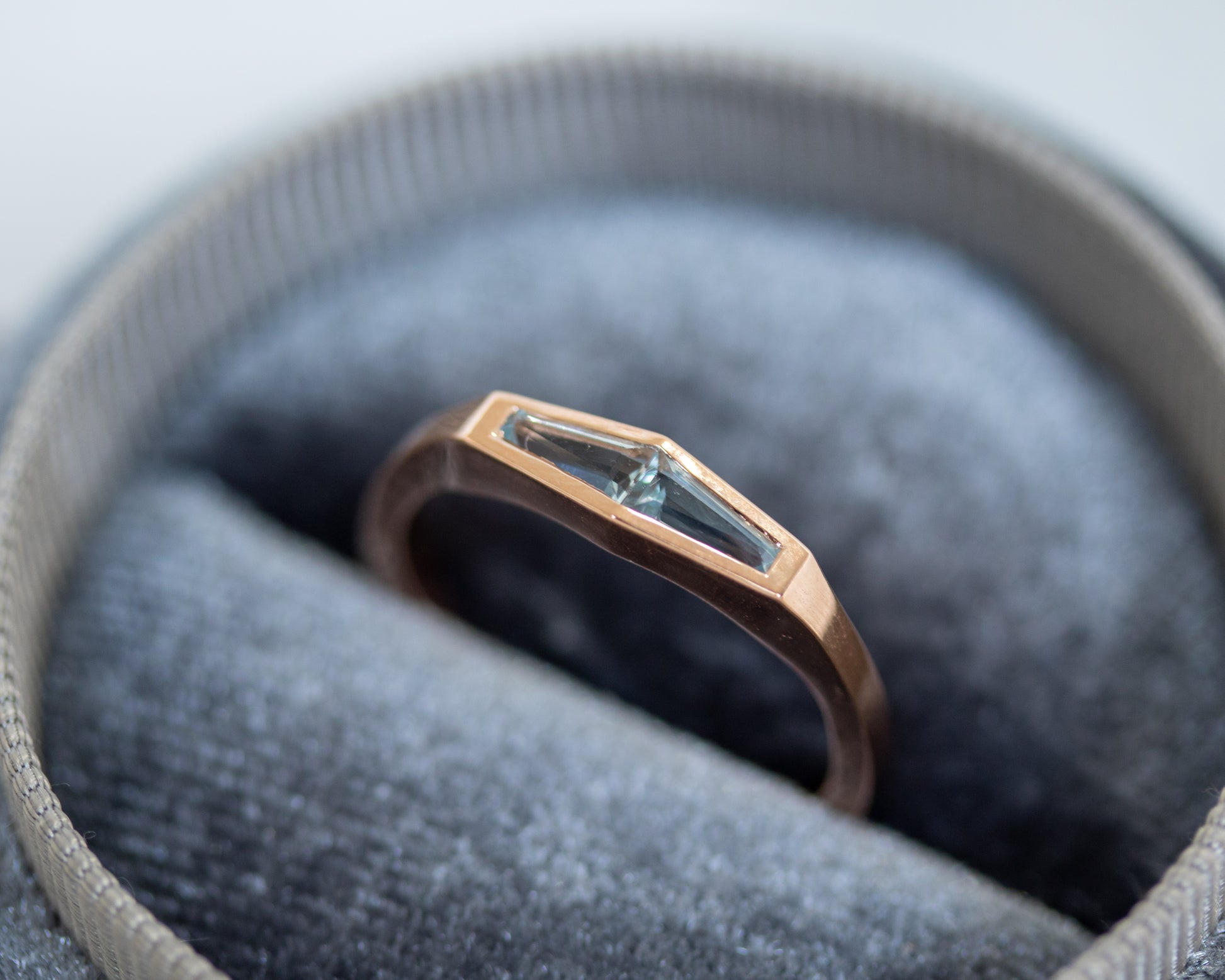 Two-stone aquamarine ring in 14K rose gold displayed on a grey stone surface