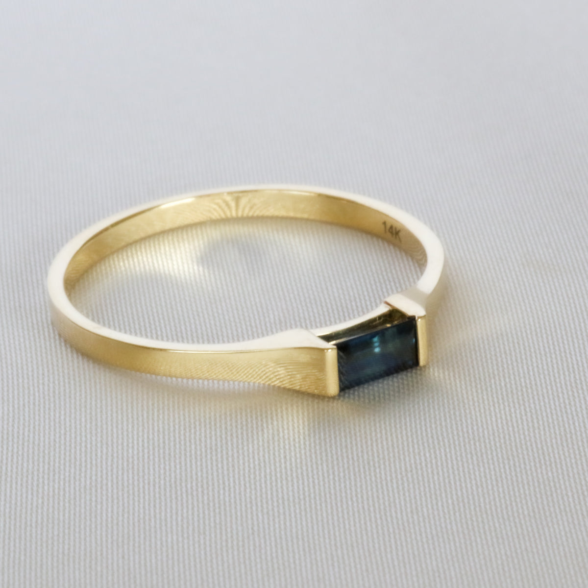 Gold band widening toward a baguette blue sapphire, angled view