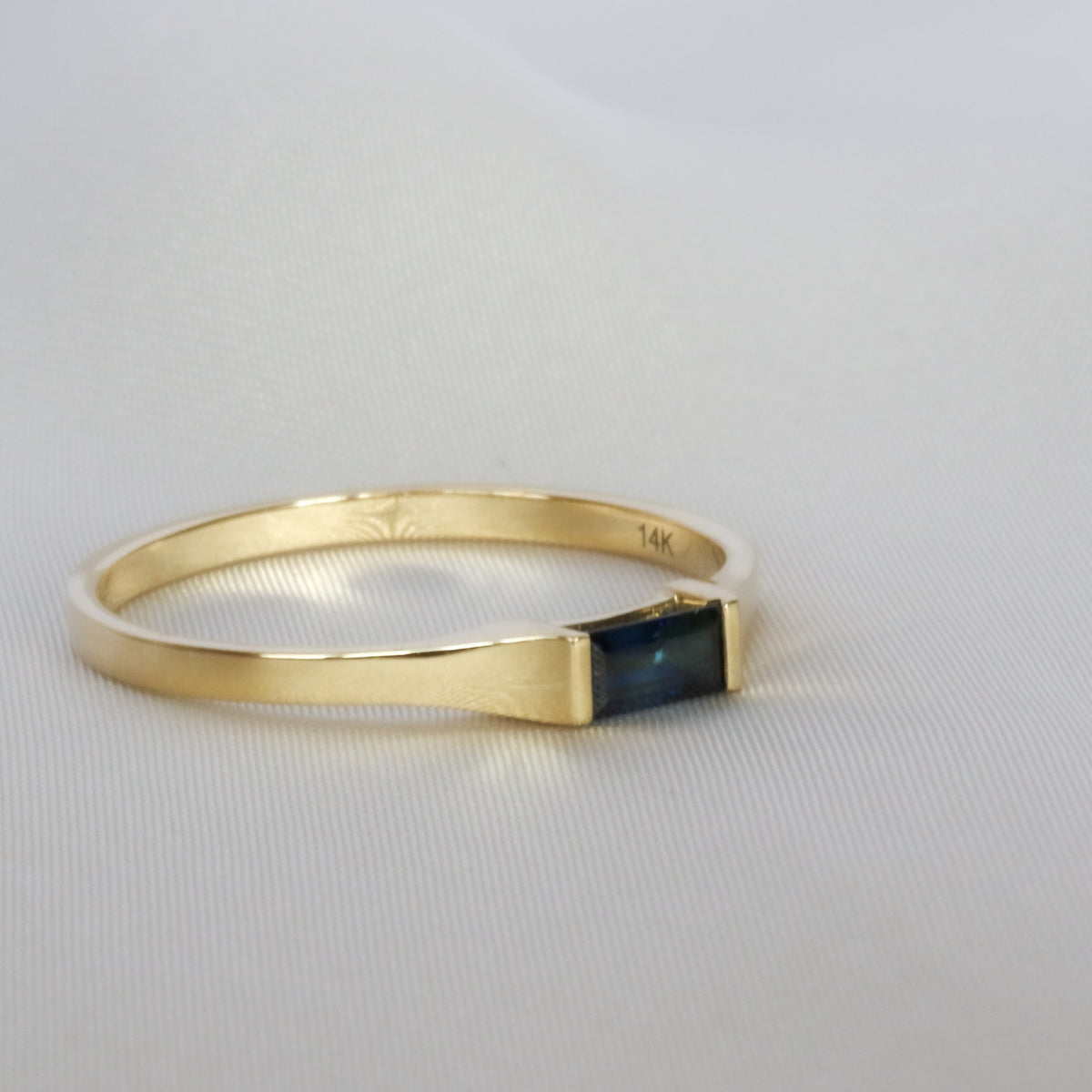 Baguette blue sapphire gold ring, side view on off-white cloth