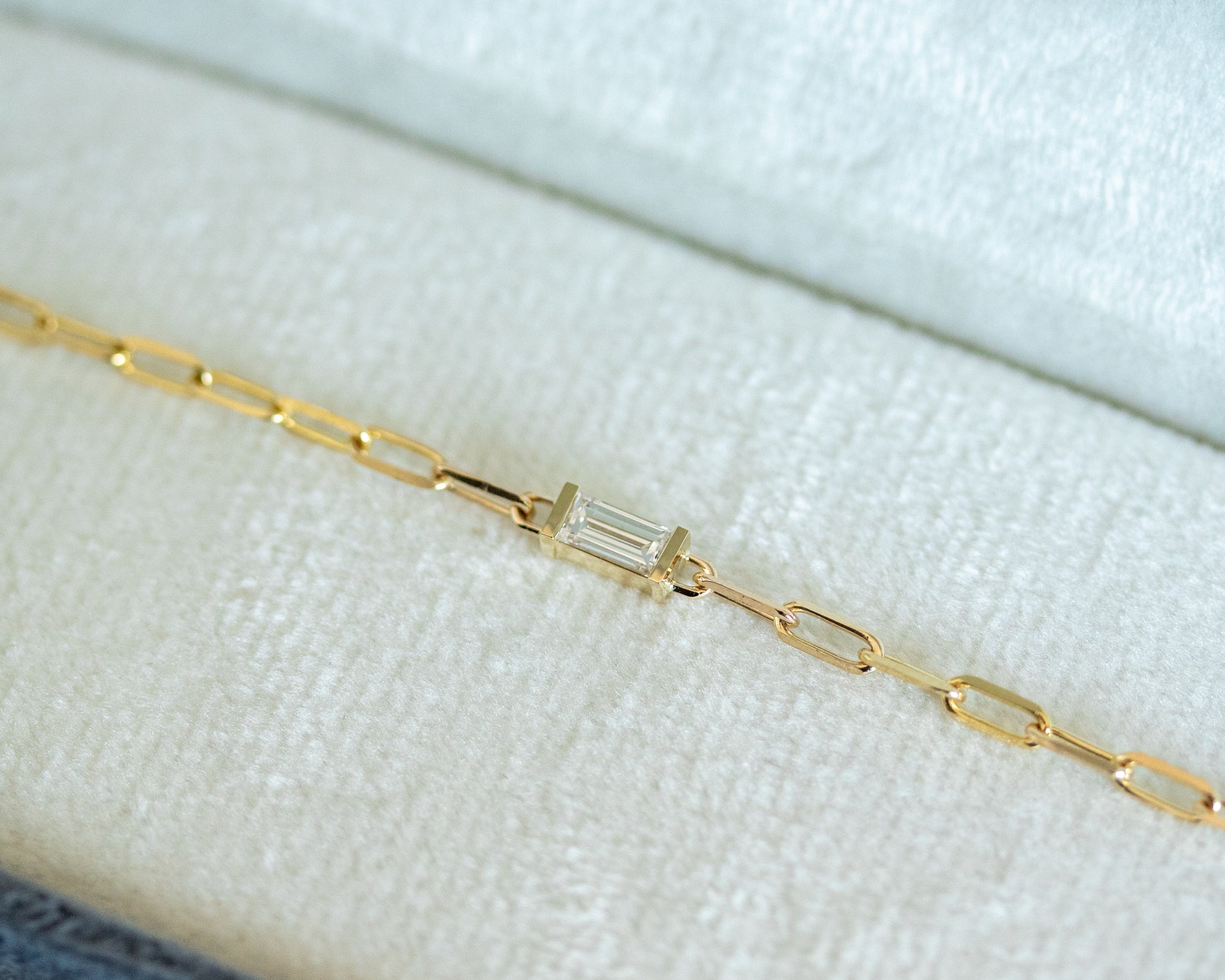 Gold bracelet with a baguette cut diamond on a light fabric background