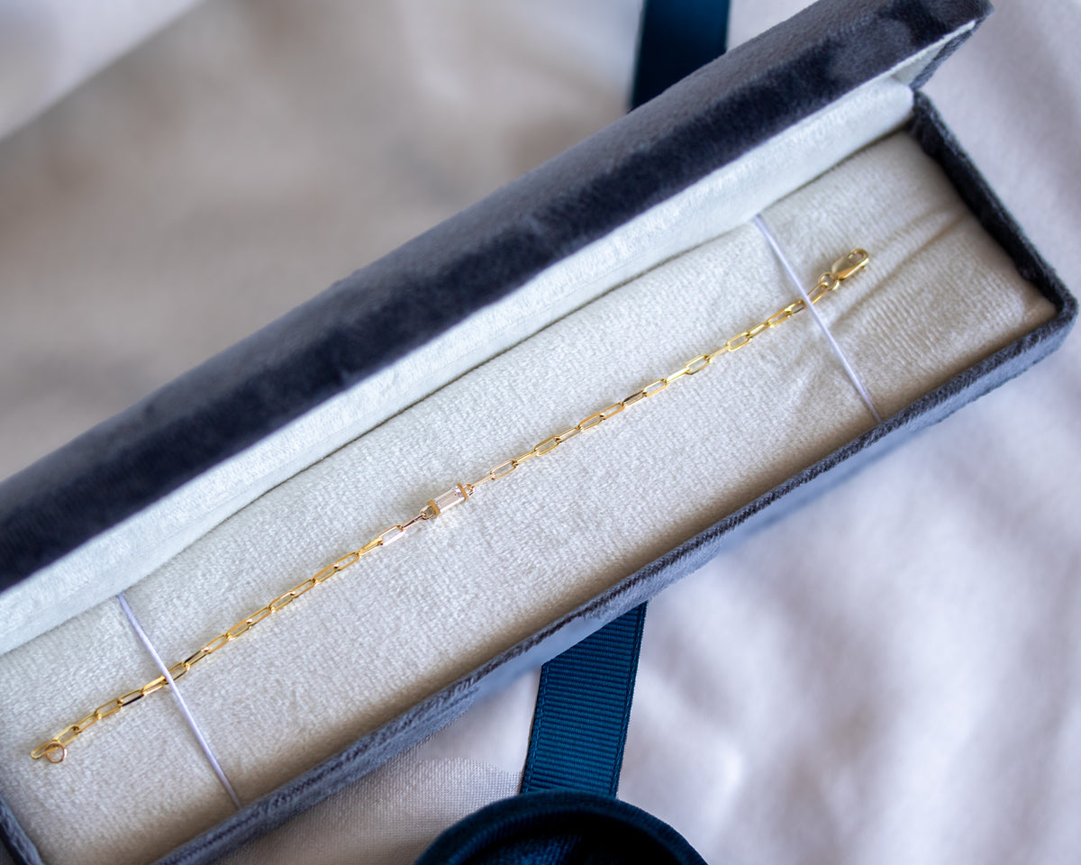 Gold paperclip chain bracelet with a baguette cut diamond in an open jewelry box