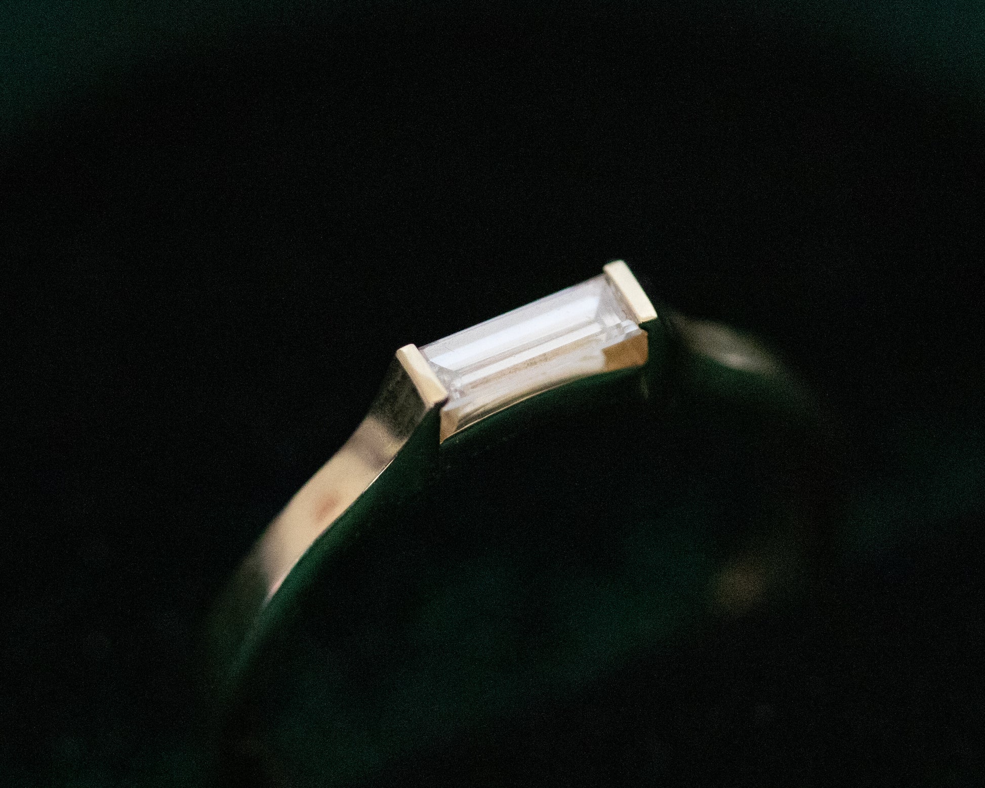 Baguette diamond gold ring on dark green backdrop