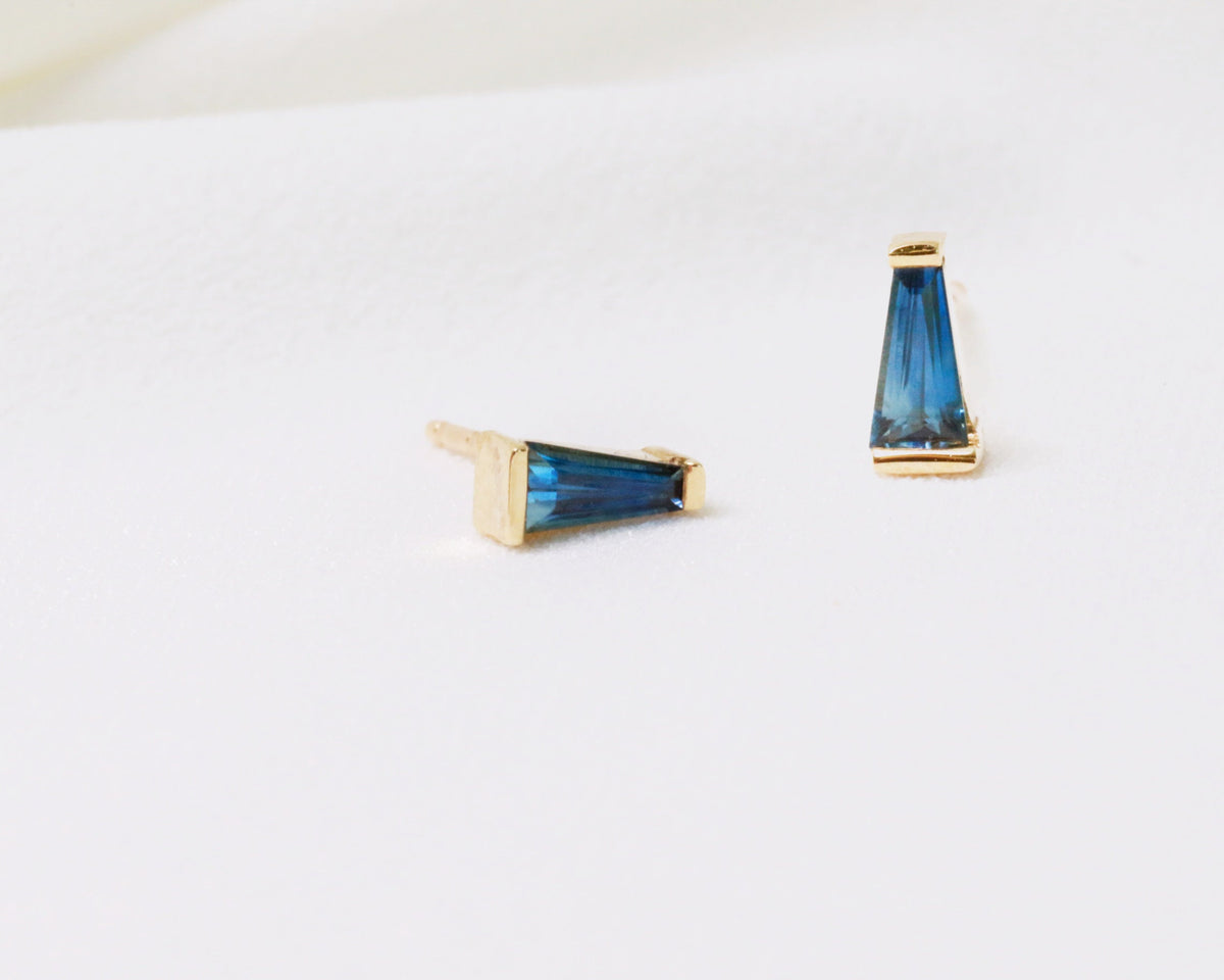 Bar-set blue tapered baguette sapphire studs in yellow gold, side and front view on white