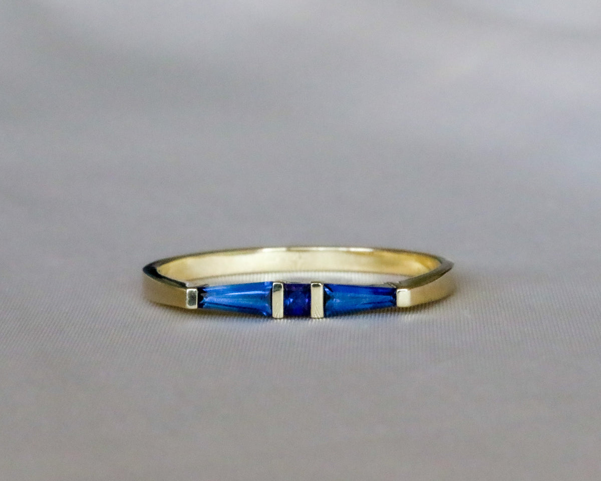 Straight-on view of three bar-set blue sapphires in a yellow gold band, gray background