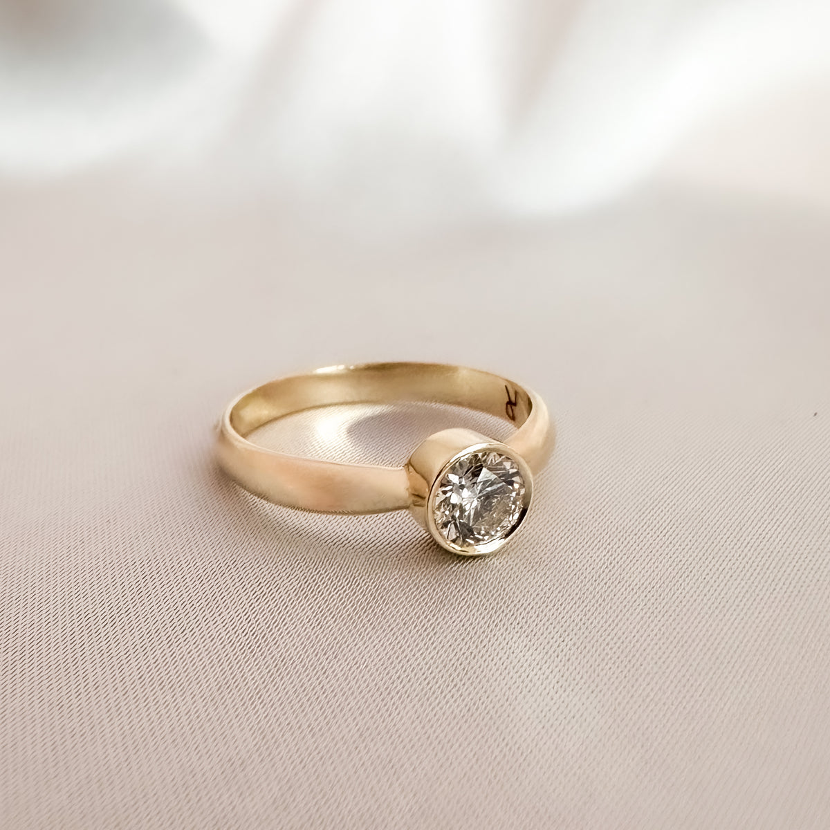 Yellow gold bezel solitaire diamond ring, side view on a light background
