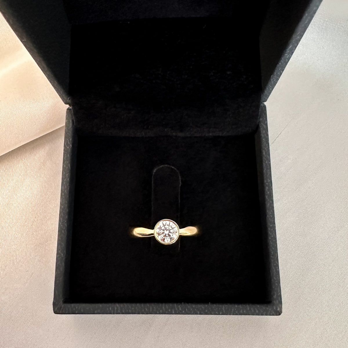 Yellow gold bezel solitaire diamond ring in a black velvet box