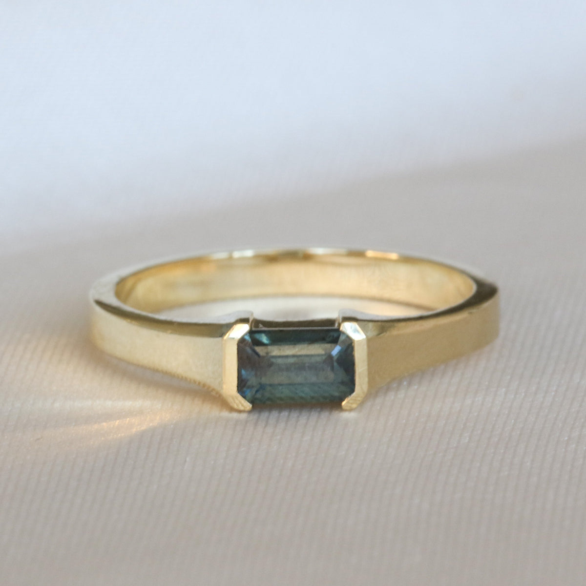 Emerald cut blue-gray sapphire half bezel ring in 14K yellow gold
