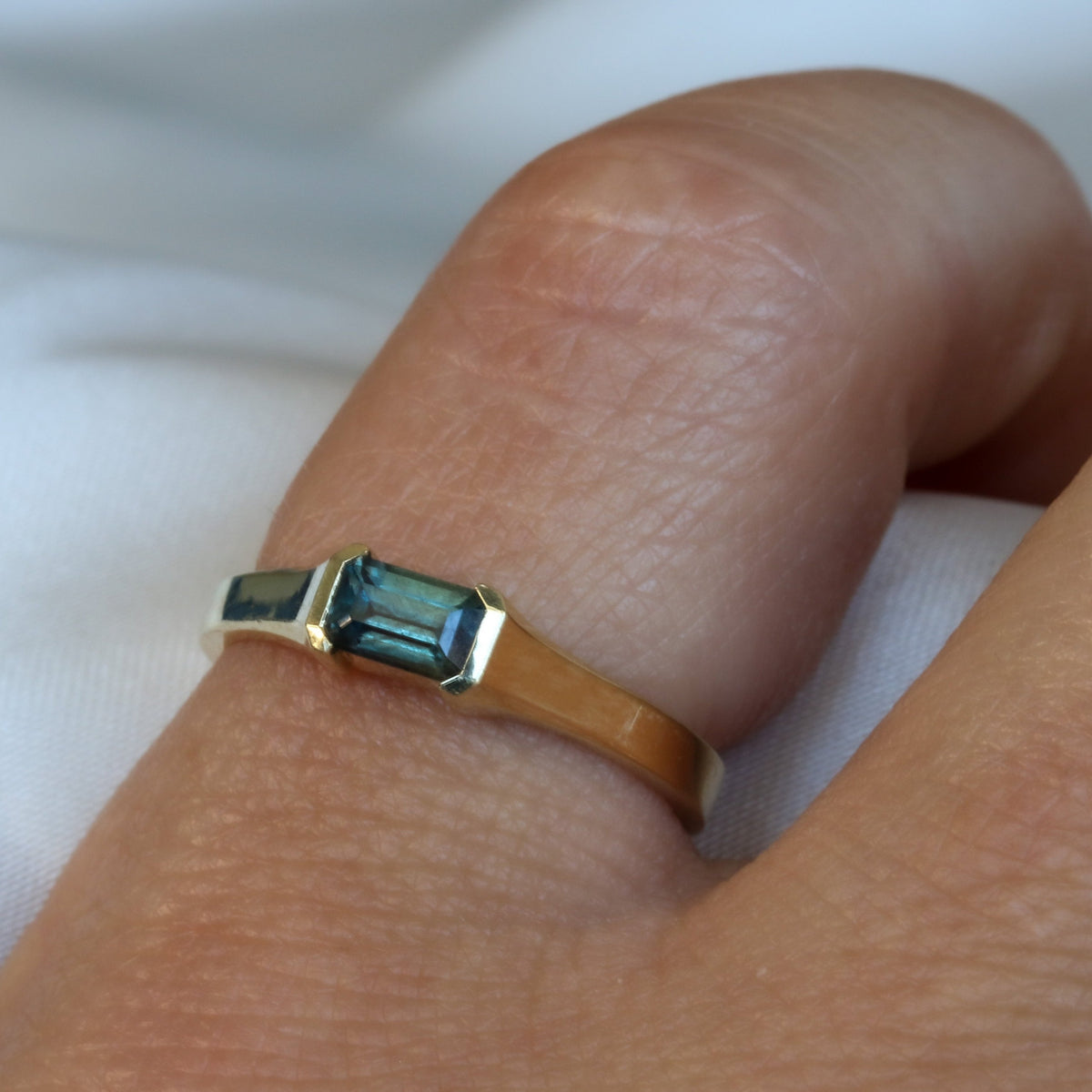Emerald cut blue-gray sapphire ring in 14K yellow gold, worn on the finger