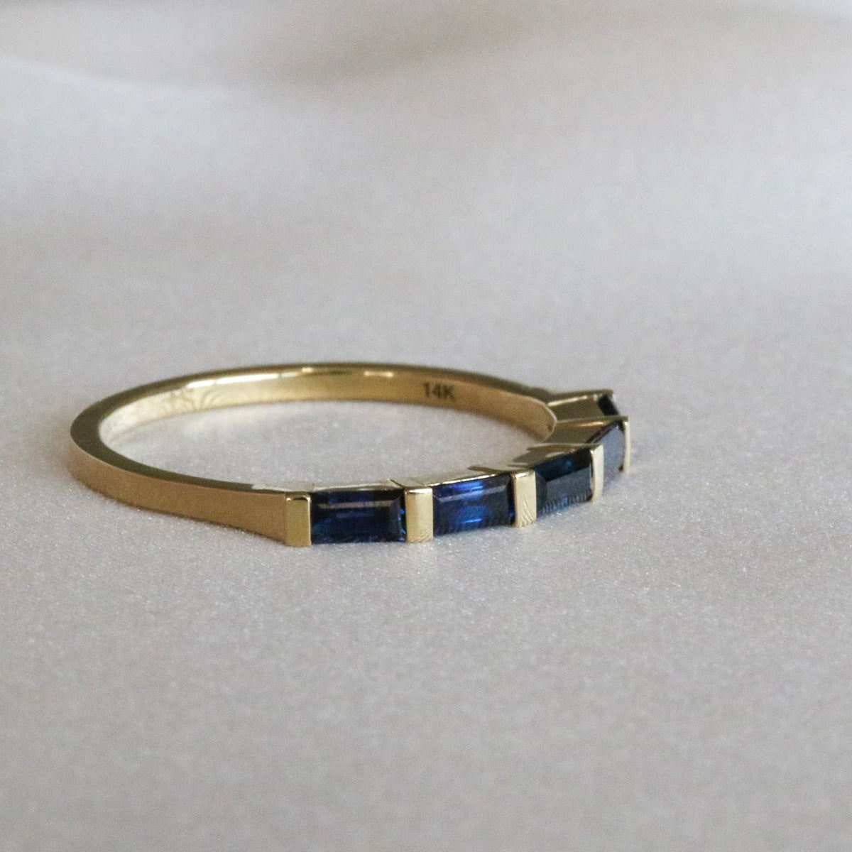 Blue sapphire baguette band in 14K yellow gold, angled view on a white surface