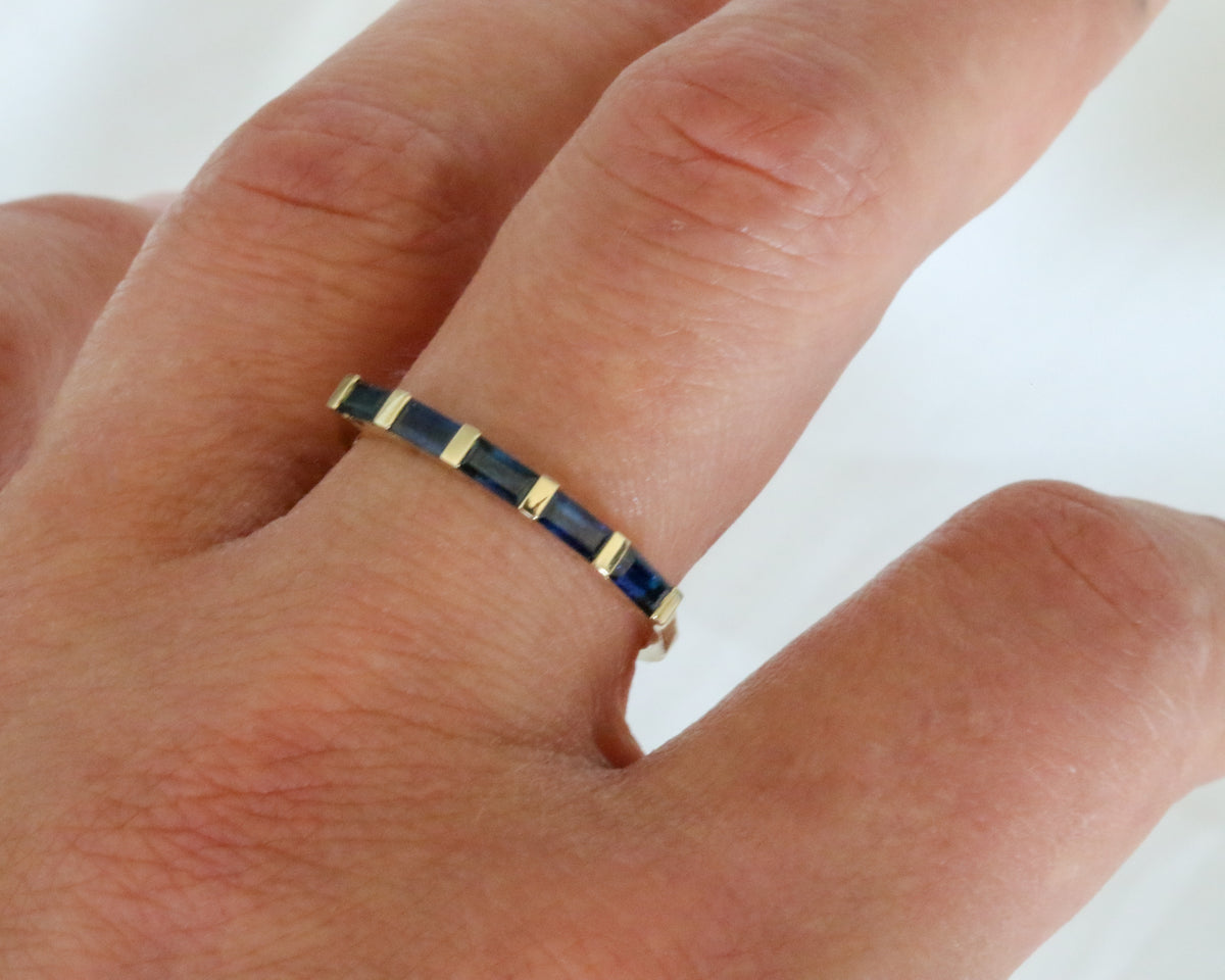 Close-up of blue sapphire baguettes in a 14K gold band on the finger