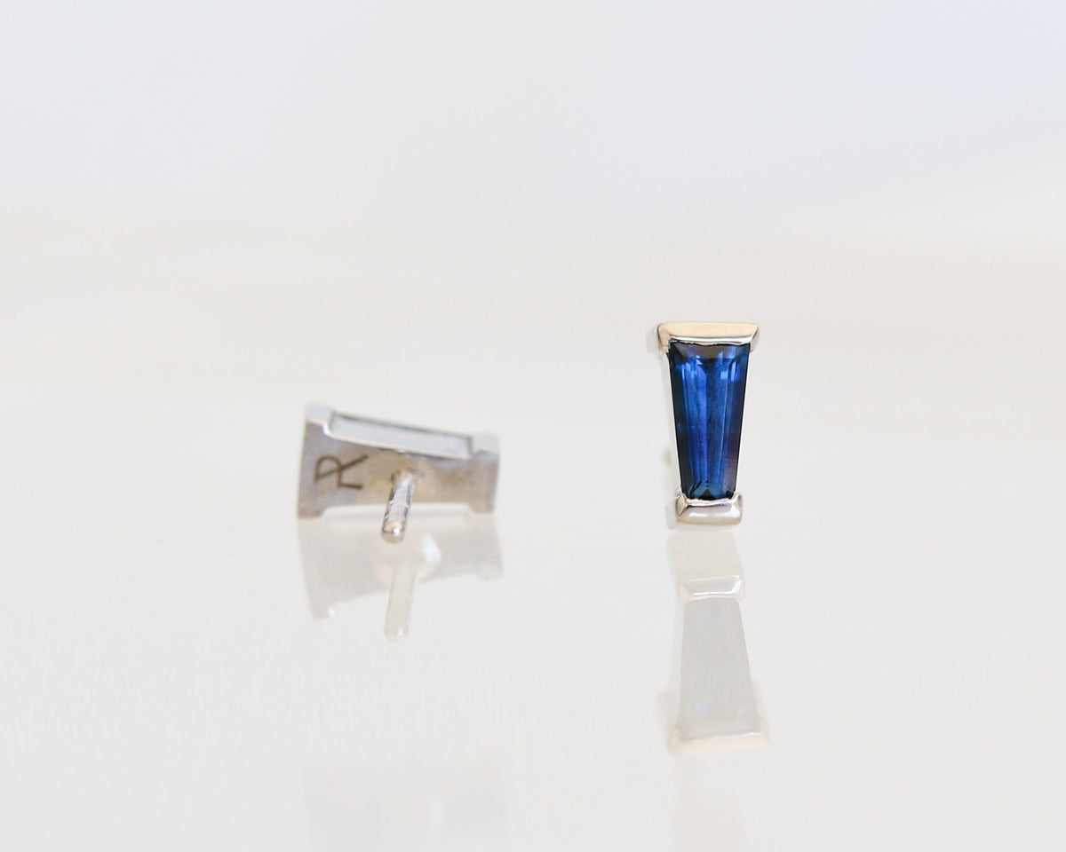 Blue tapered baguette sapphire stud earrings in white gold, one shown from the back with the post