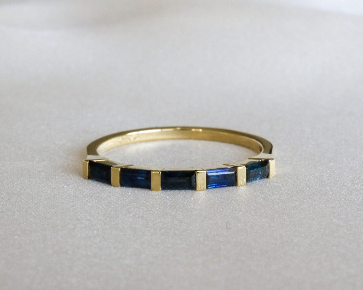 Five natural blue sapphire baguettes bar-set east-west in a 14K gold ring on a gray background