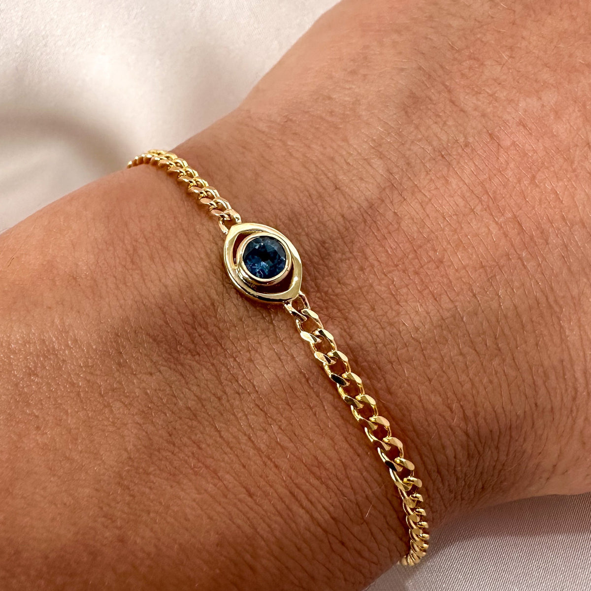 Close-up of a 14K yellow gold blue sapphire evil eye curb chain bracelet on the wrist