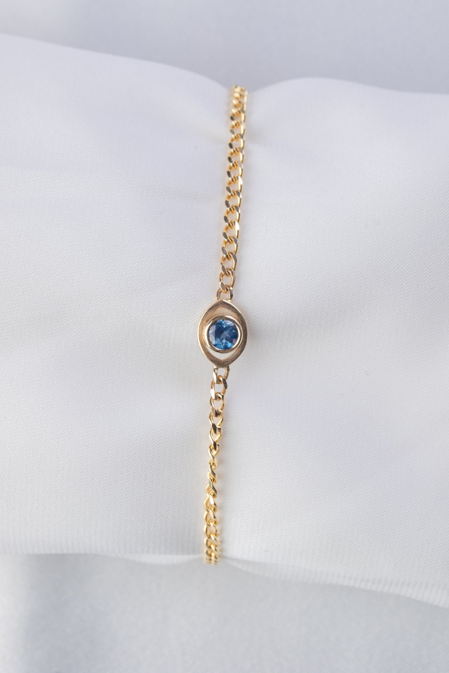 Gold bracelet with evil eye charm and  a blue sapphire on a white background