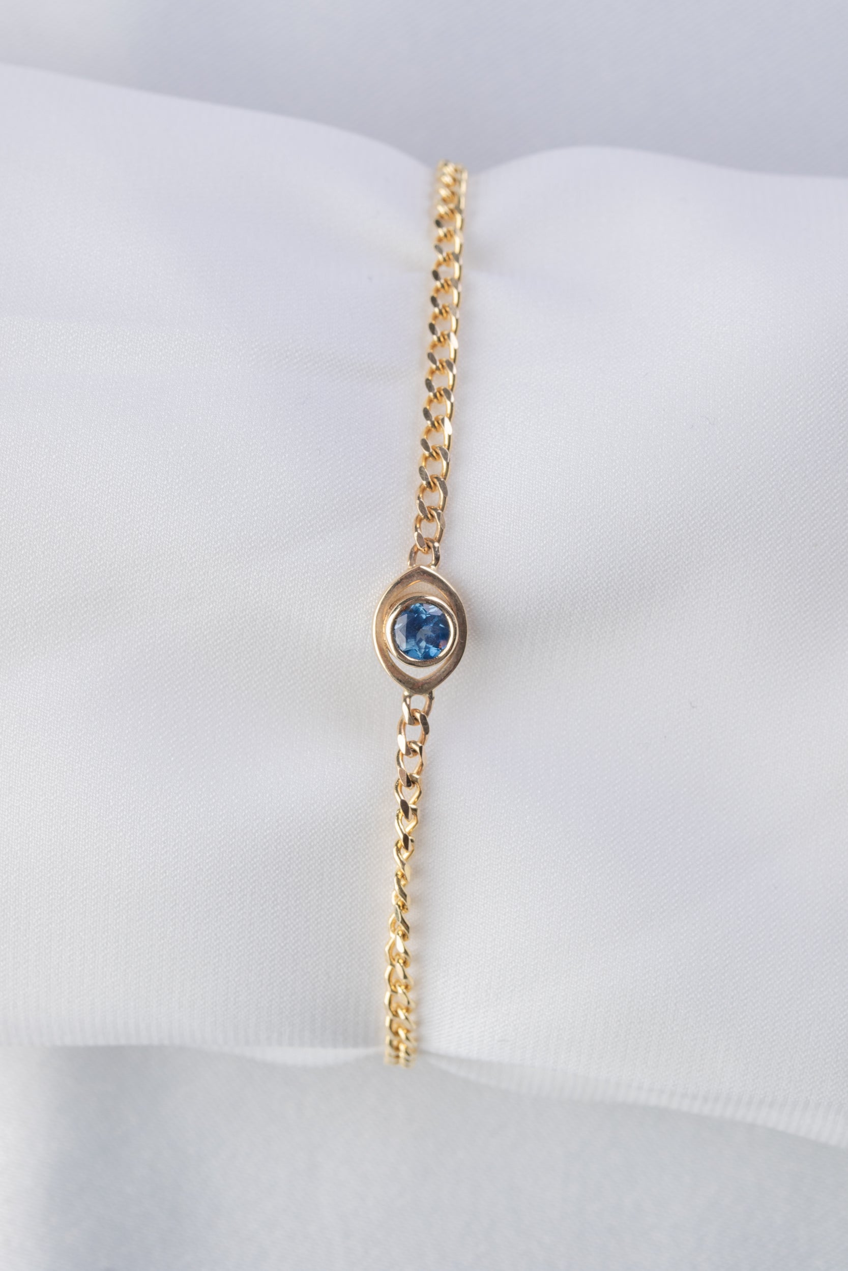 Gold bracelet with evil eye charm and  a blue sapphire on a white background