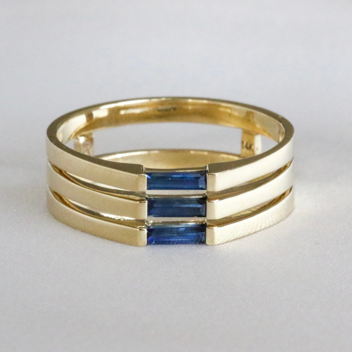 14K yellow gold three-stone ring with needle baguette blue sapphires set east-west, angled front view