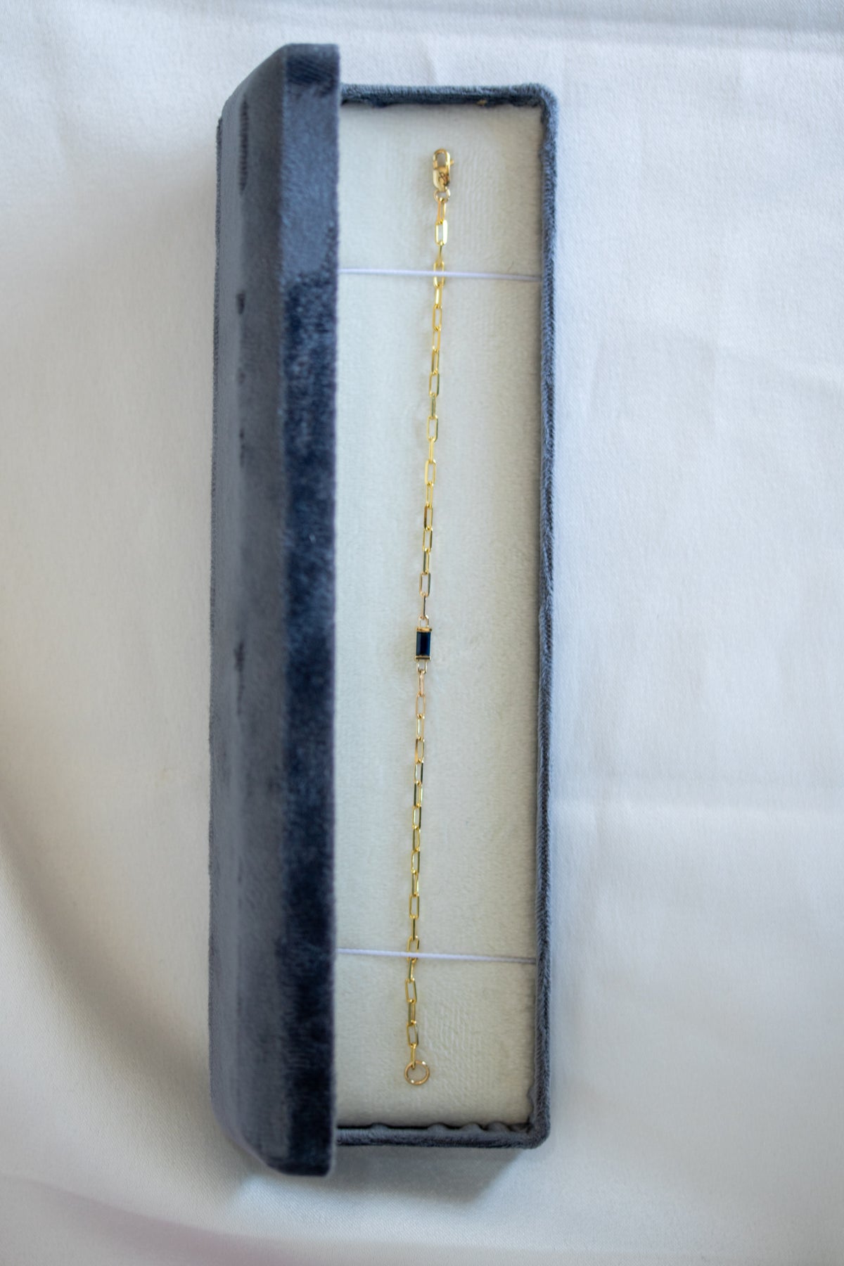 Blue sapphire paperclip chain bracelet laid in a long gray jewelry box