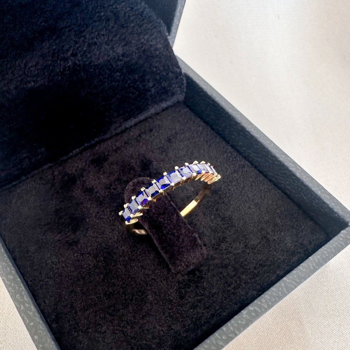 Princess cut blue sapphire band in 14K yellow gold in an open black velvet box