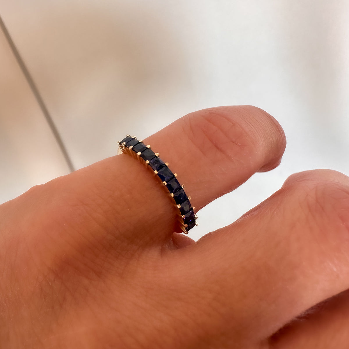 Close-up of princess cut royal blue sapphires set edge to edge in a 14K yellow gold band on the finger