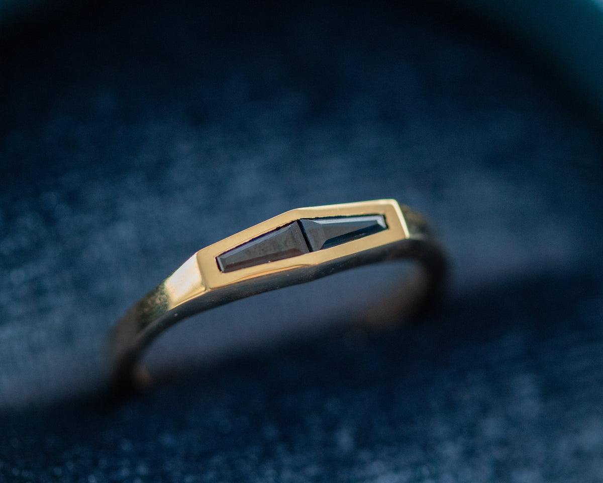 Two-stone tapered baguette blue sapphire ring in 14K yellow gold, resting on deep blue fabric.