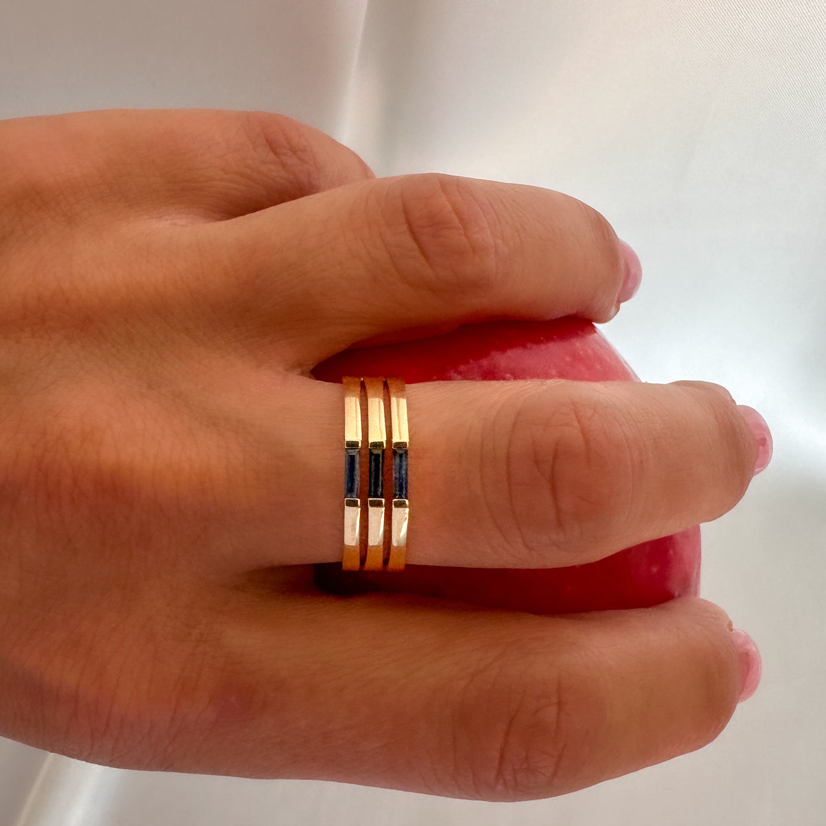 Yellow gold three-stone blue sapphire ring worn on the finger, against a red background