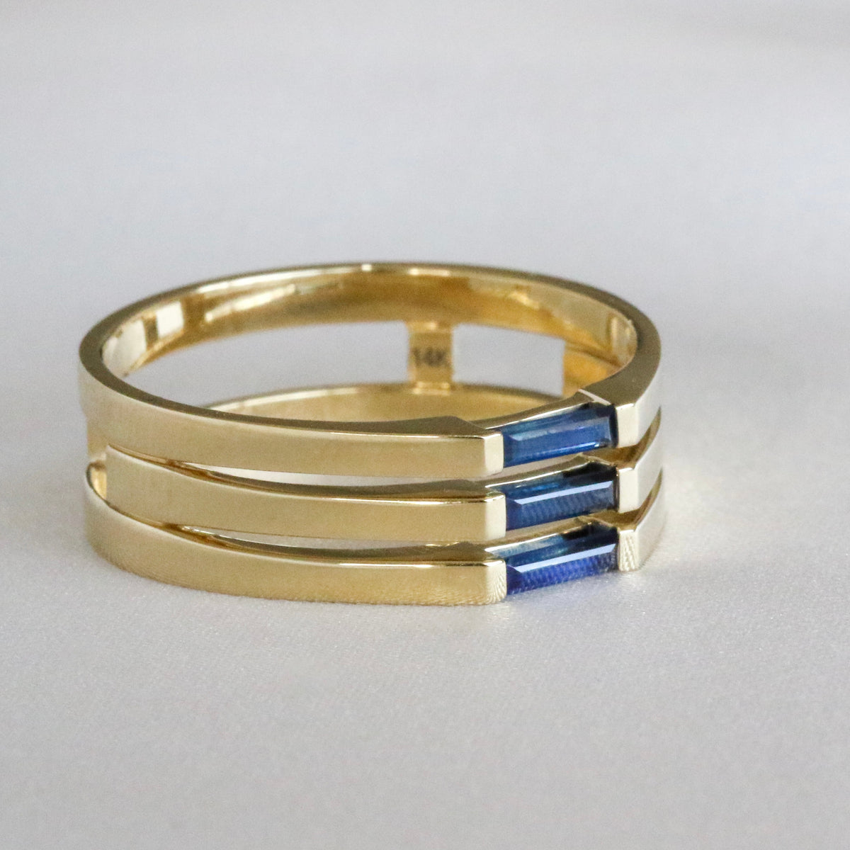 Side angle of a 14K yellow gold three-stone ring with needle baguette blue sapphires