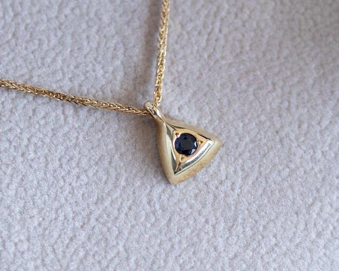 Triangle blue sapphire pendant necklace in gold, resting in an open gift box with dried flowers