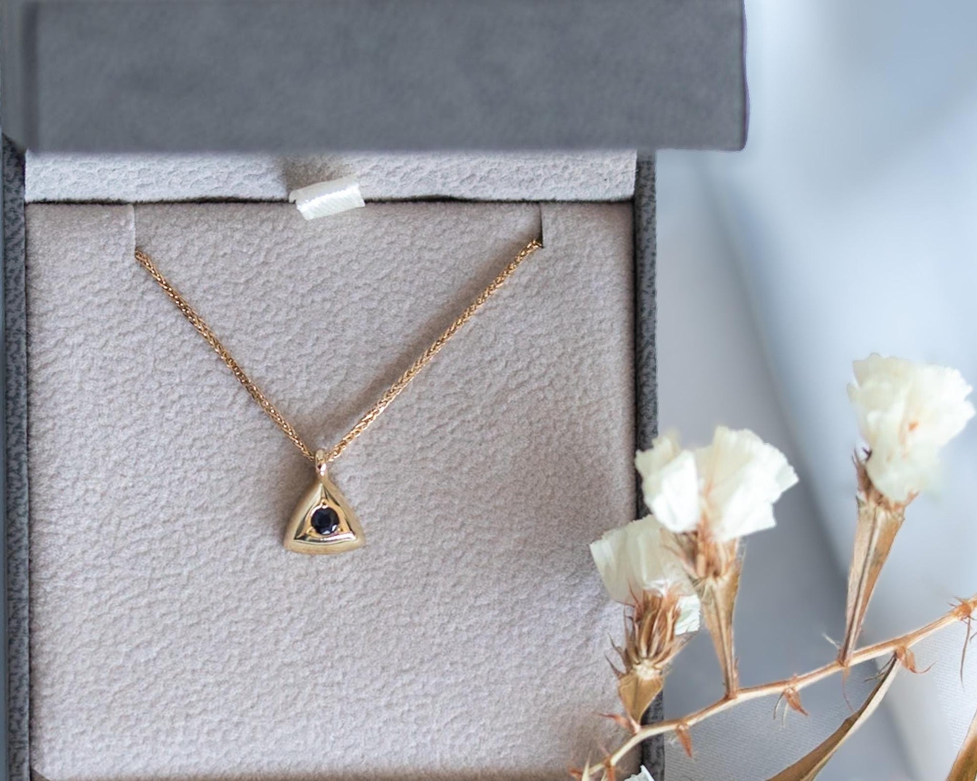 Gold triangle pendant with a blue sapphire, displayed in a jewelry gift box