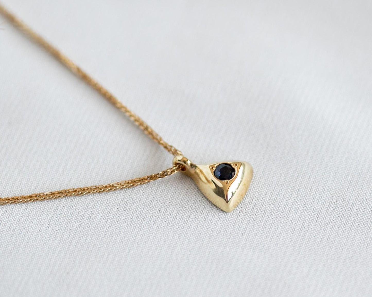Gold triangle pendant with a round blue sapphire and a delicate chain on a white background