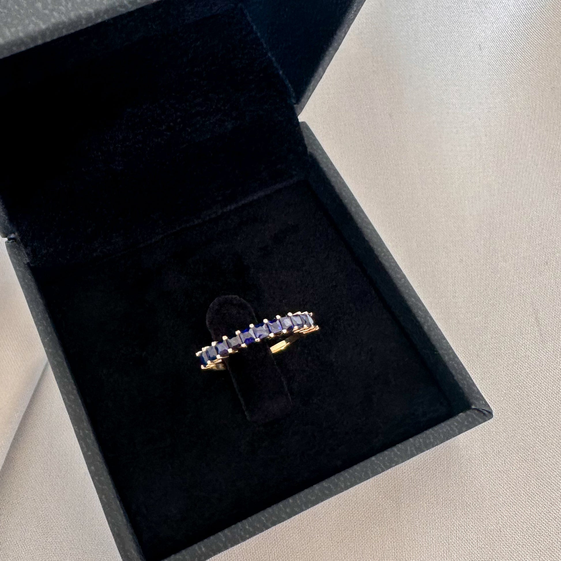  princess cut blue sapphire eternity ring displayed in black velvet box