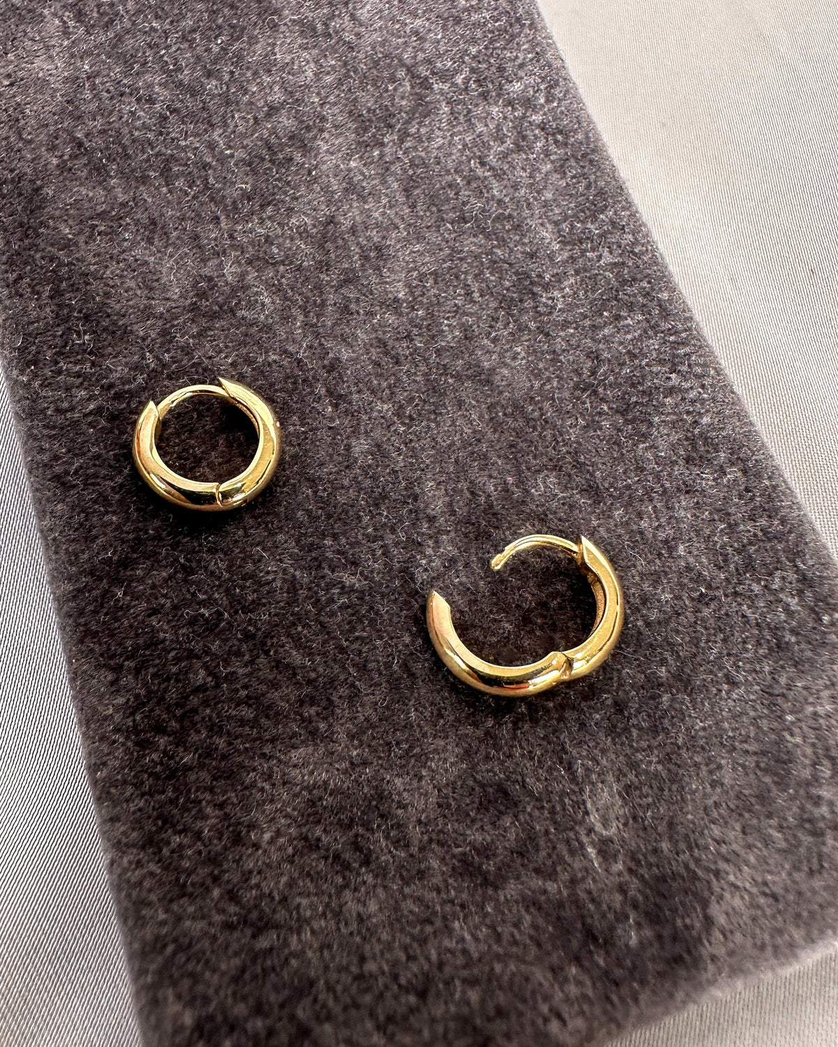 Small chunky yellow gold hoop earrings on grey fabric, one open showing the wrap closure