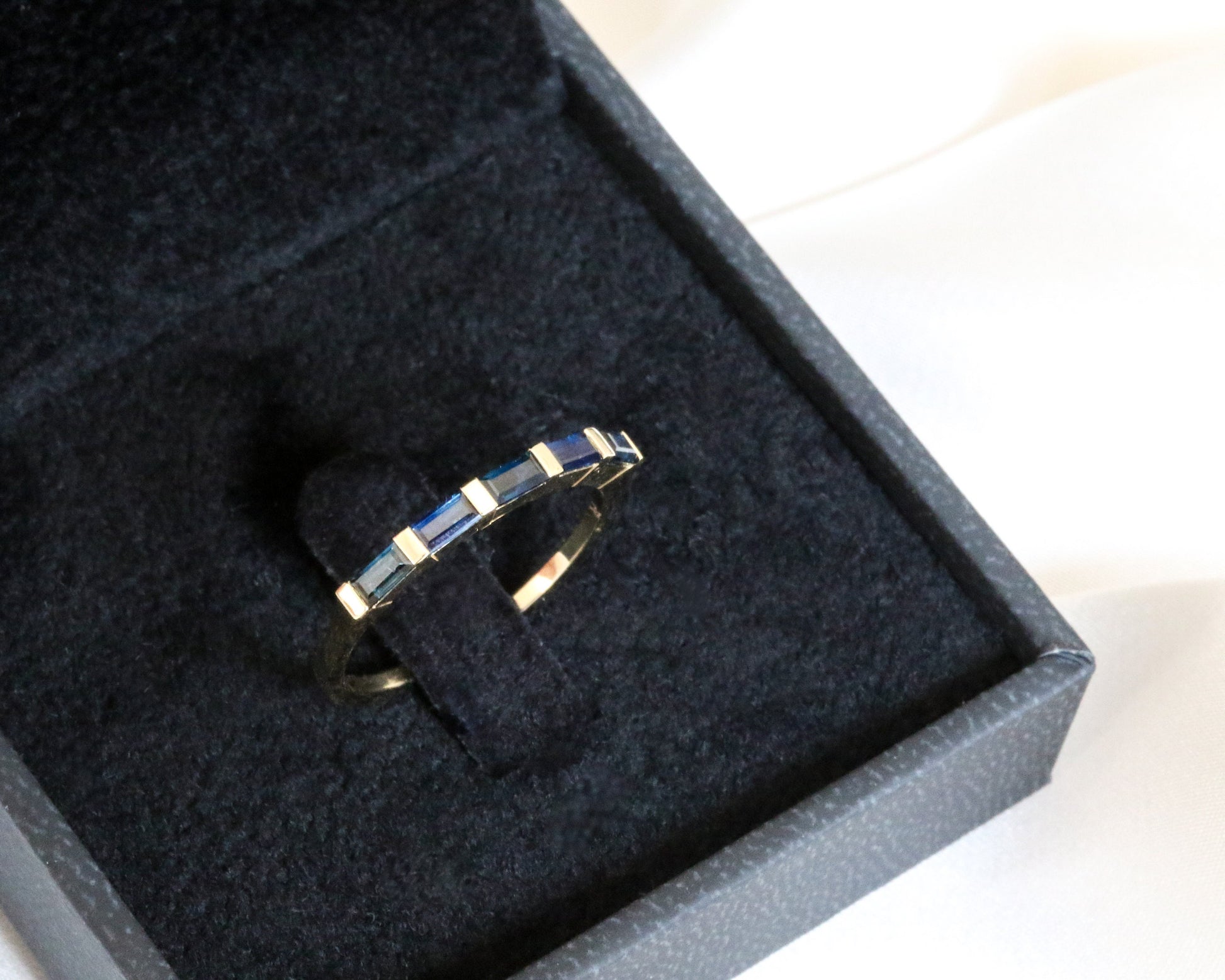 Close-up of 14K gold blue sapphire baguette ring on black velvet jewelry box — elegant minimalist stacking ring