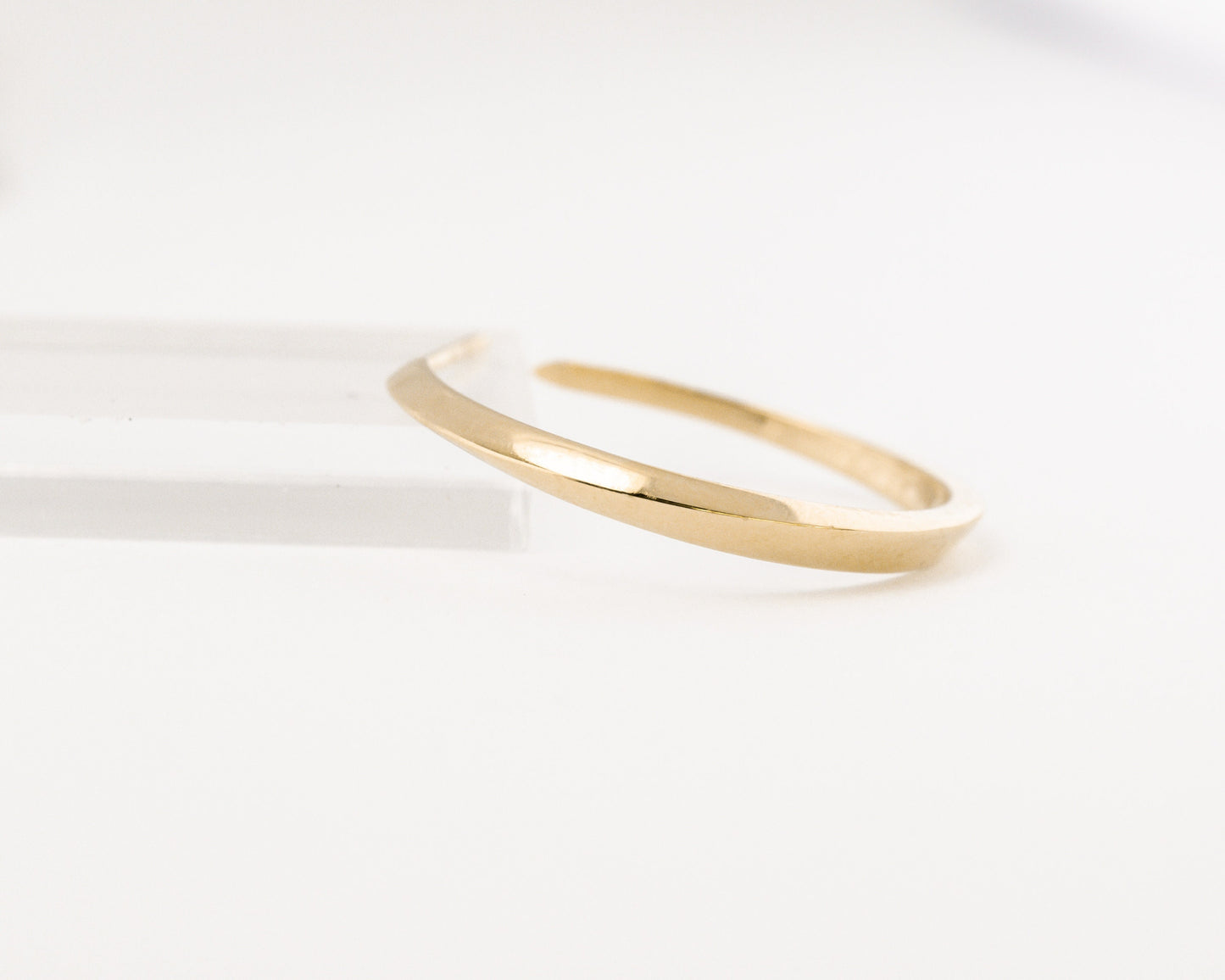 Close-up of a 14K gold geometric hoop earring from the Twist collection, showing the smooth polished finish and minimalist sculptural curve on white background.