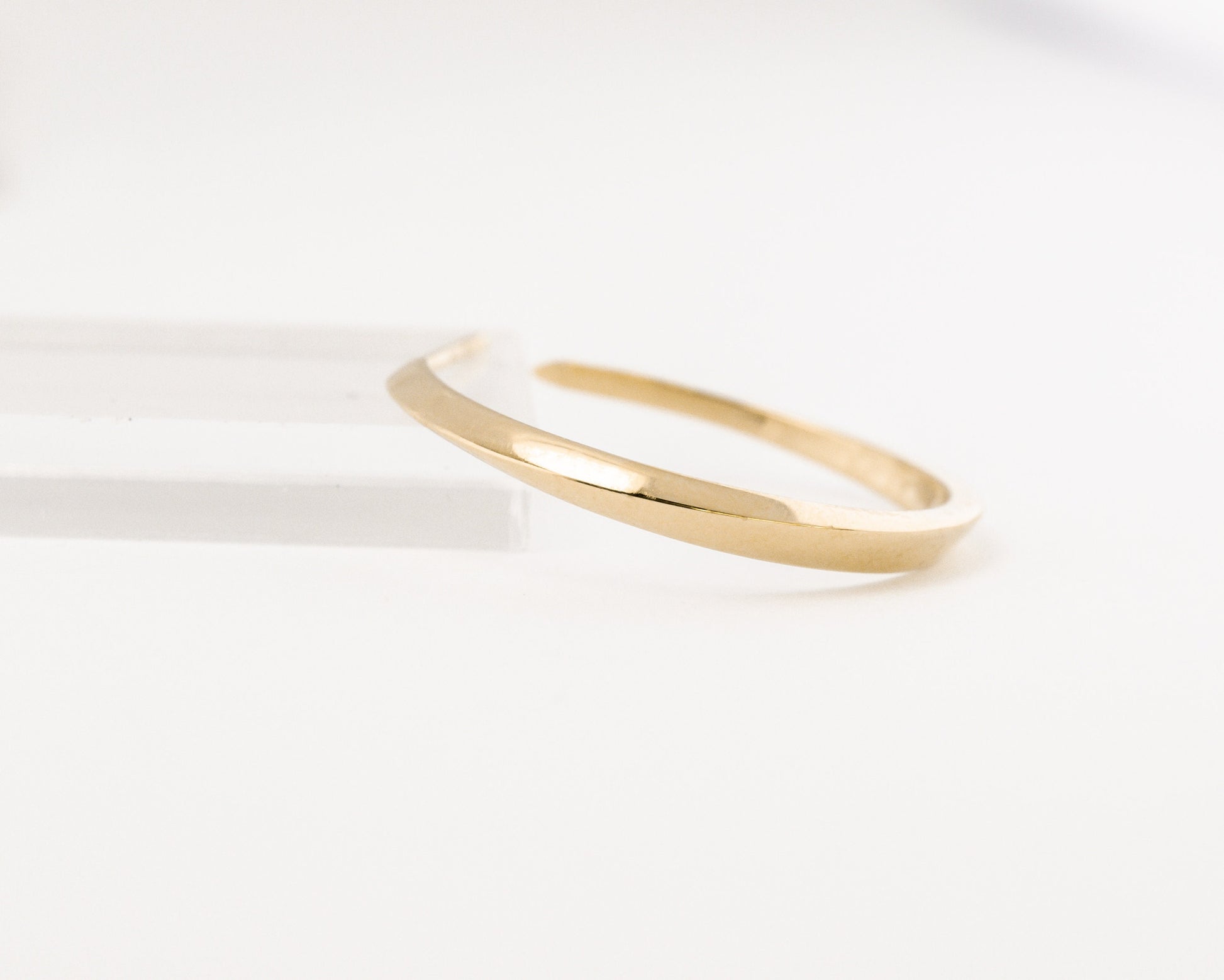 Close-up of a 14K gold geometric hoop earring from the Twist collection, showing the smooth polished finish and minimalist sculptural curve on white background.