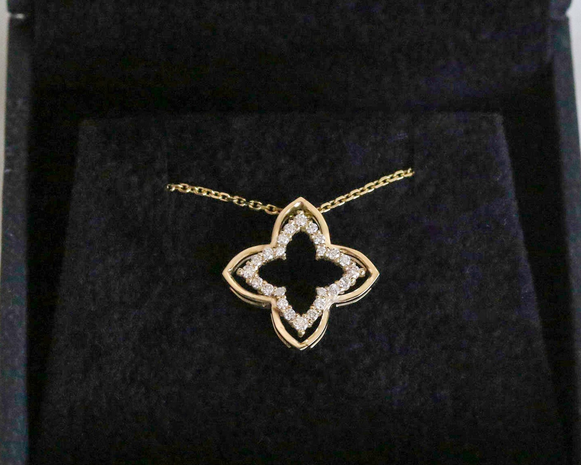 Gold necklace with a clover-shaped pendant on a black background