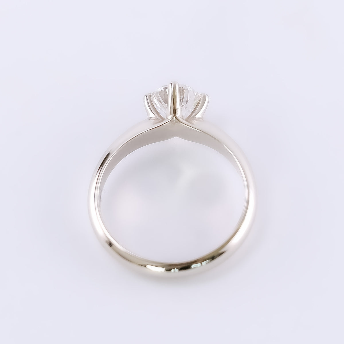 White gold solitaire ring standing upright, showing four compass prongs around a round diamond