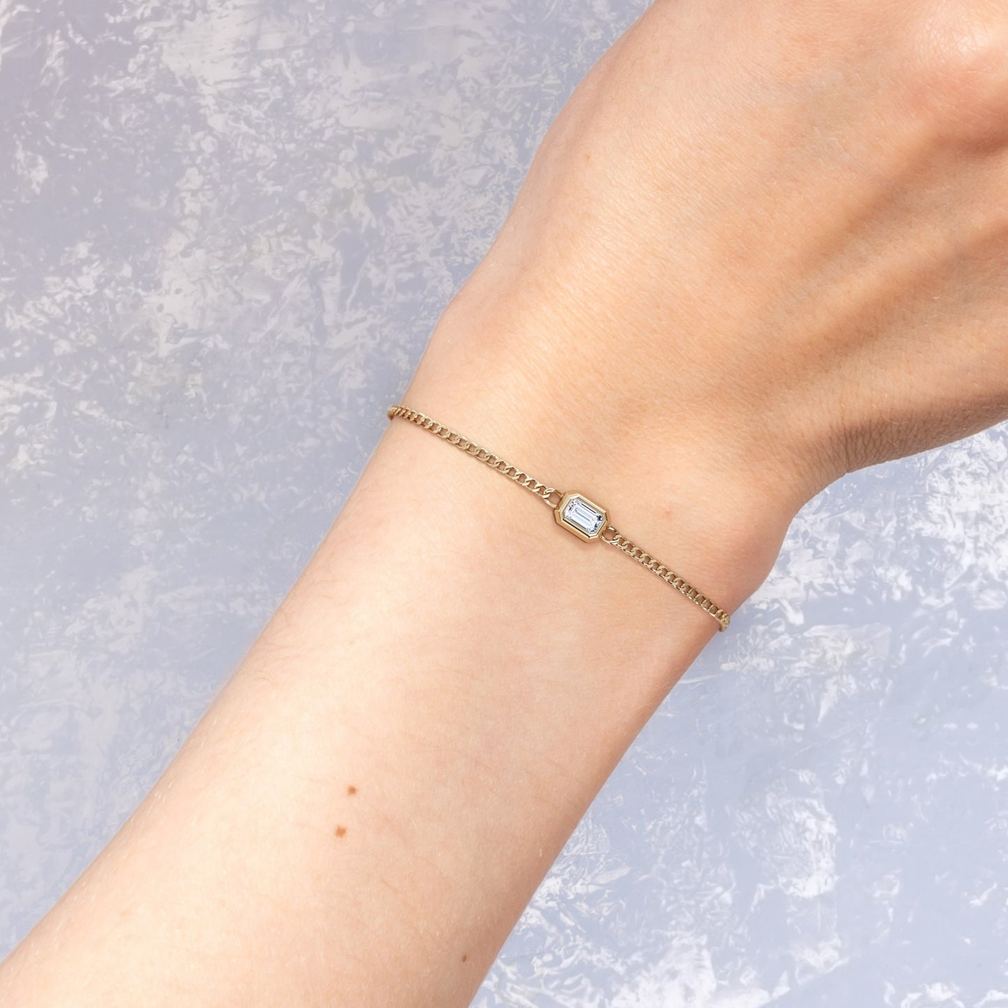14K yellow gold curb chain bracelet with emerald cut diamond worn on the wrist