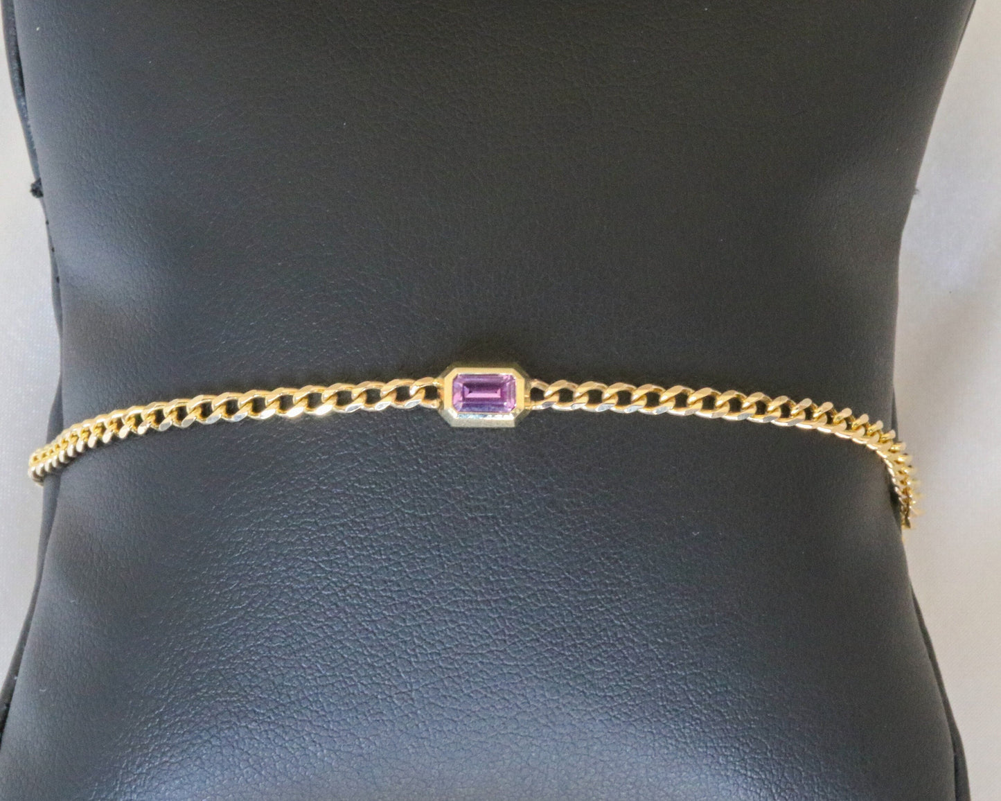 14K yellow gold curb chain bracelet with emerald cut pink sapphire on a display stand