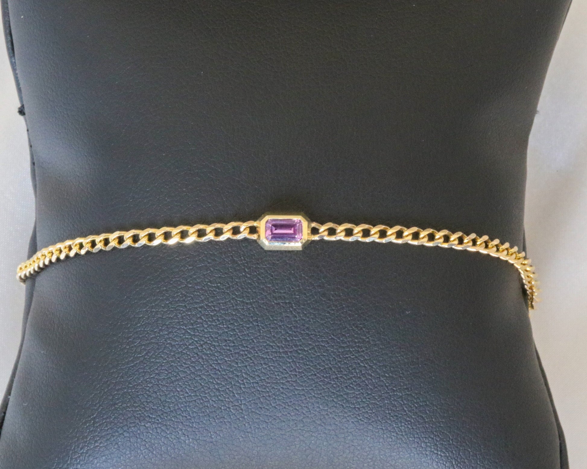 14K yellow gold curb chain bracelet with emerald cut pink sapphire on a display stand