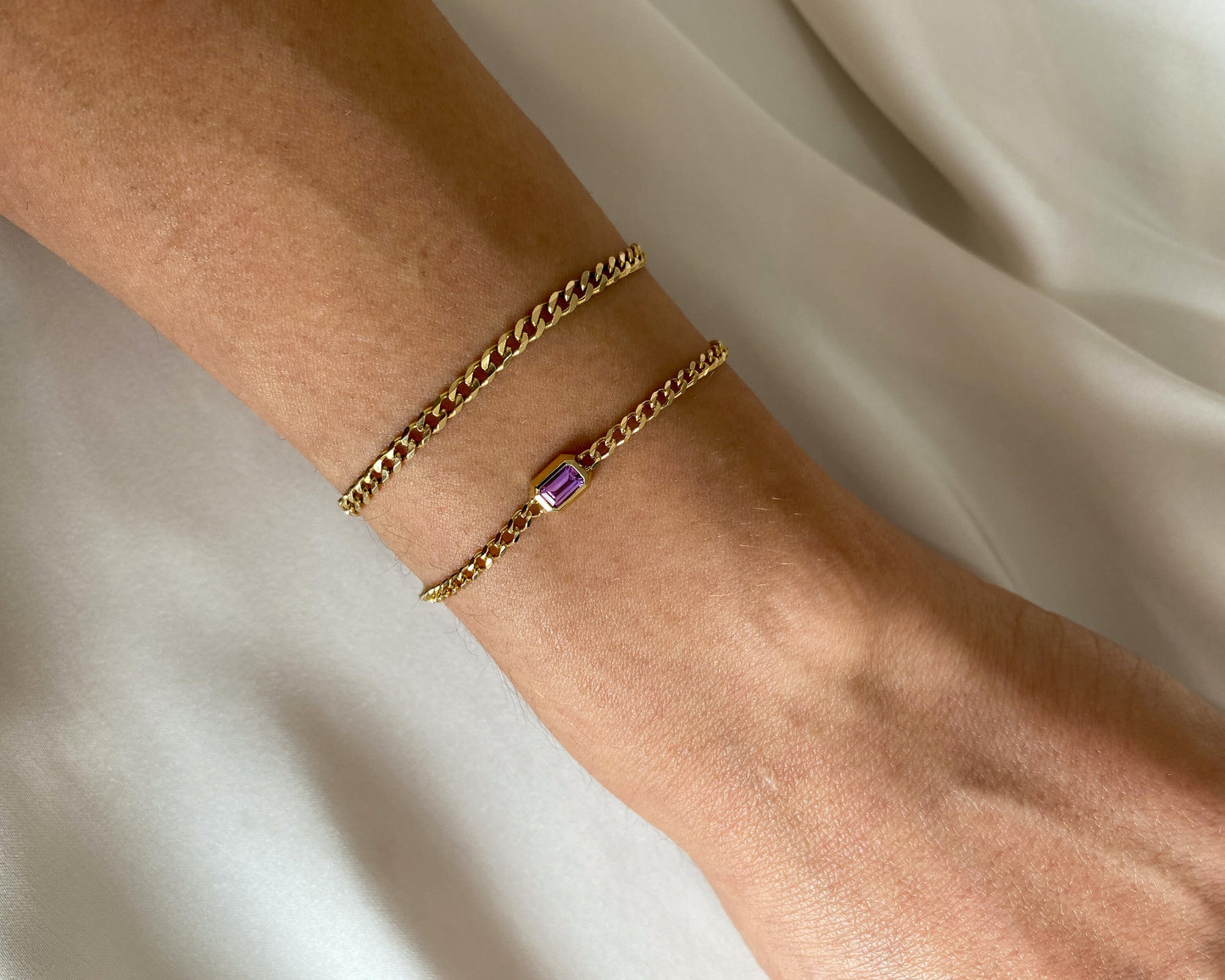 14K yellow gold curb chain bracelet with emerald cut pink sapphire layered on the wrist