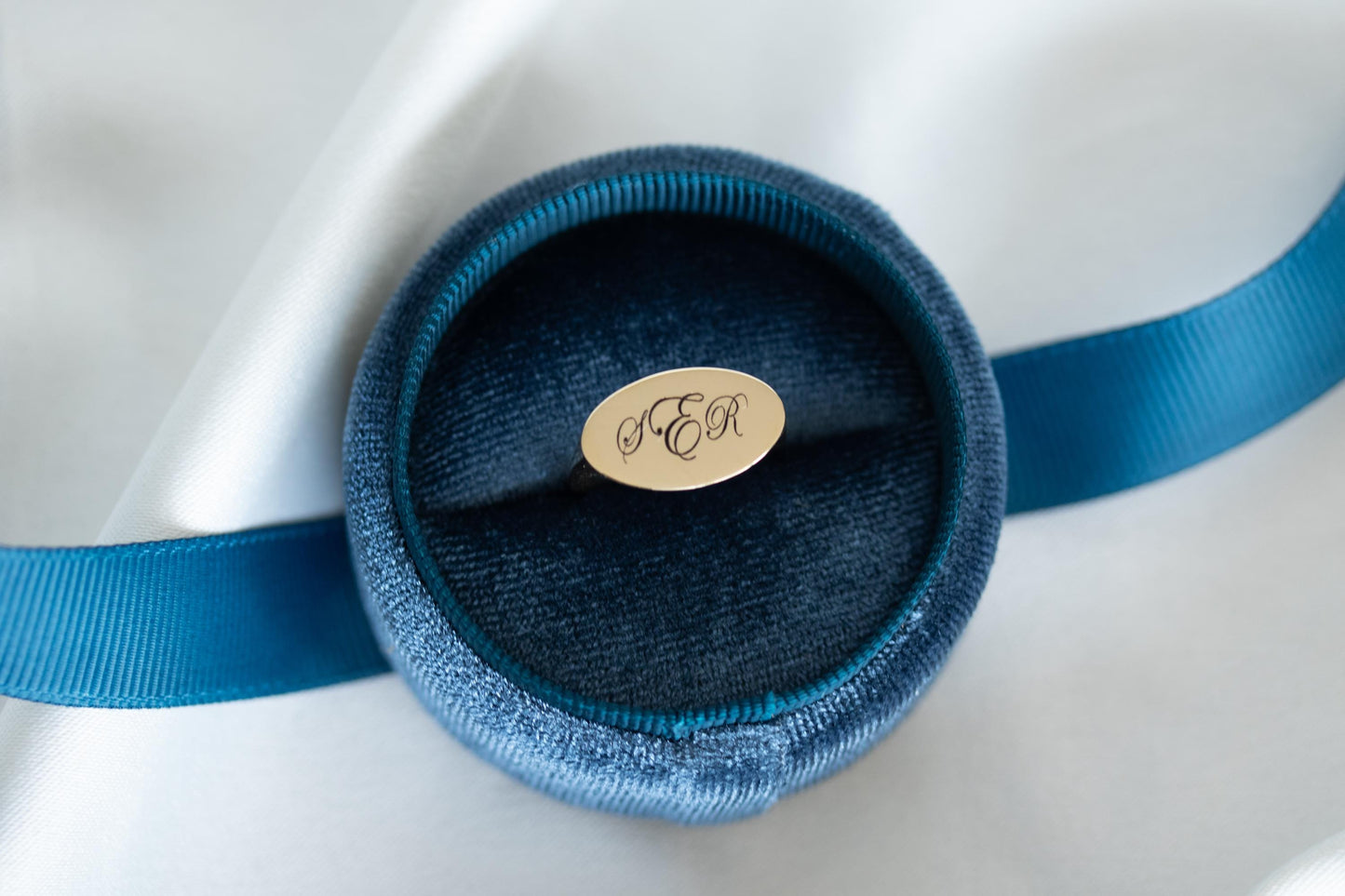 Blue velvet ring box with a gold monogram on a white satin surface