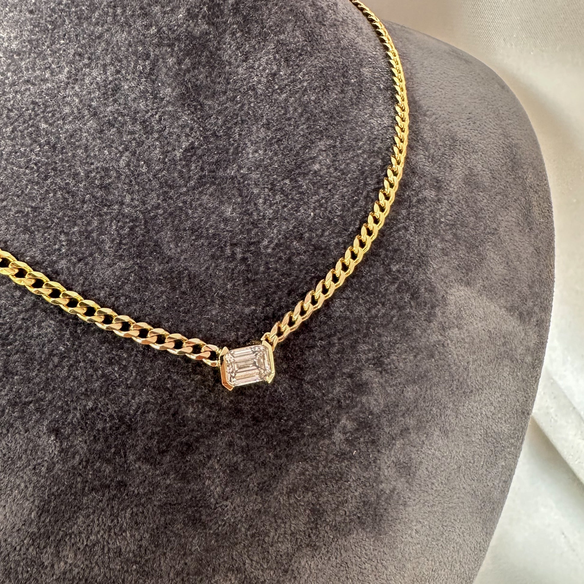 A 14K gold diamond solitaire necklace with an emerald cut natural diamond pendant on a gray textured jewelry torso