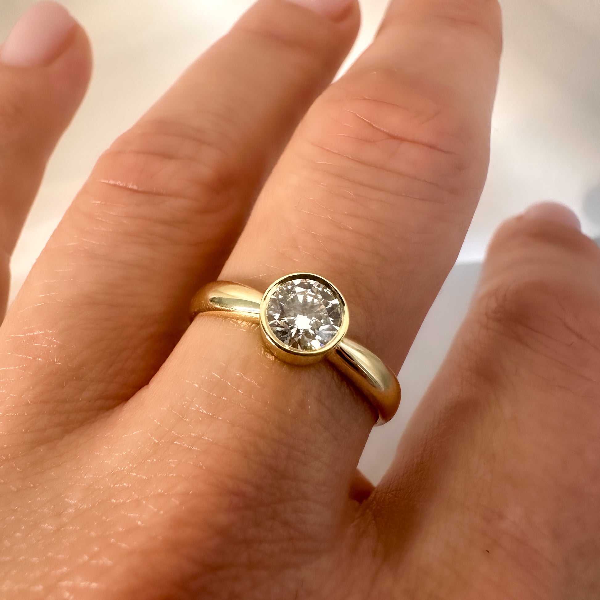 close up of gold solitaire ring with bezel setting on hand