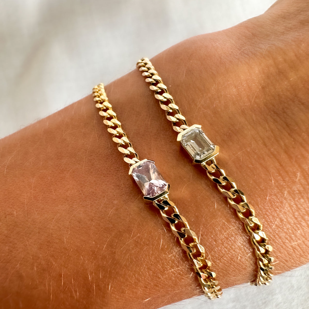 Emerald cut diamond and pink sapphire curb chain bracelets in 14K gold, worn on the wrist