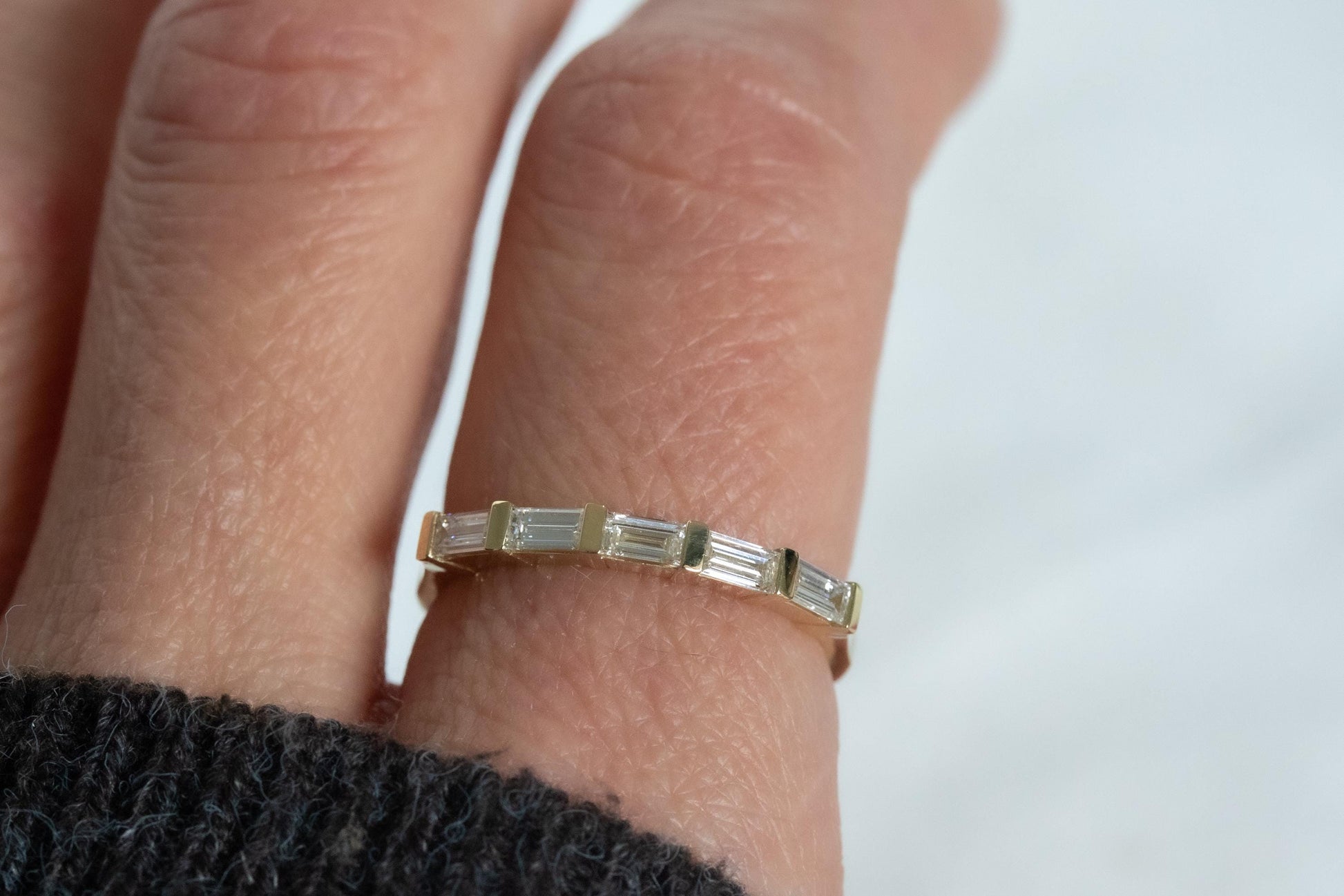 Gold ring with baguette diamonds on a finger against a white background