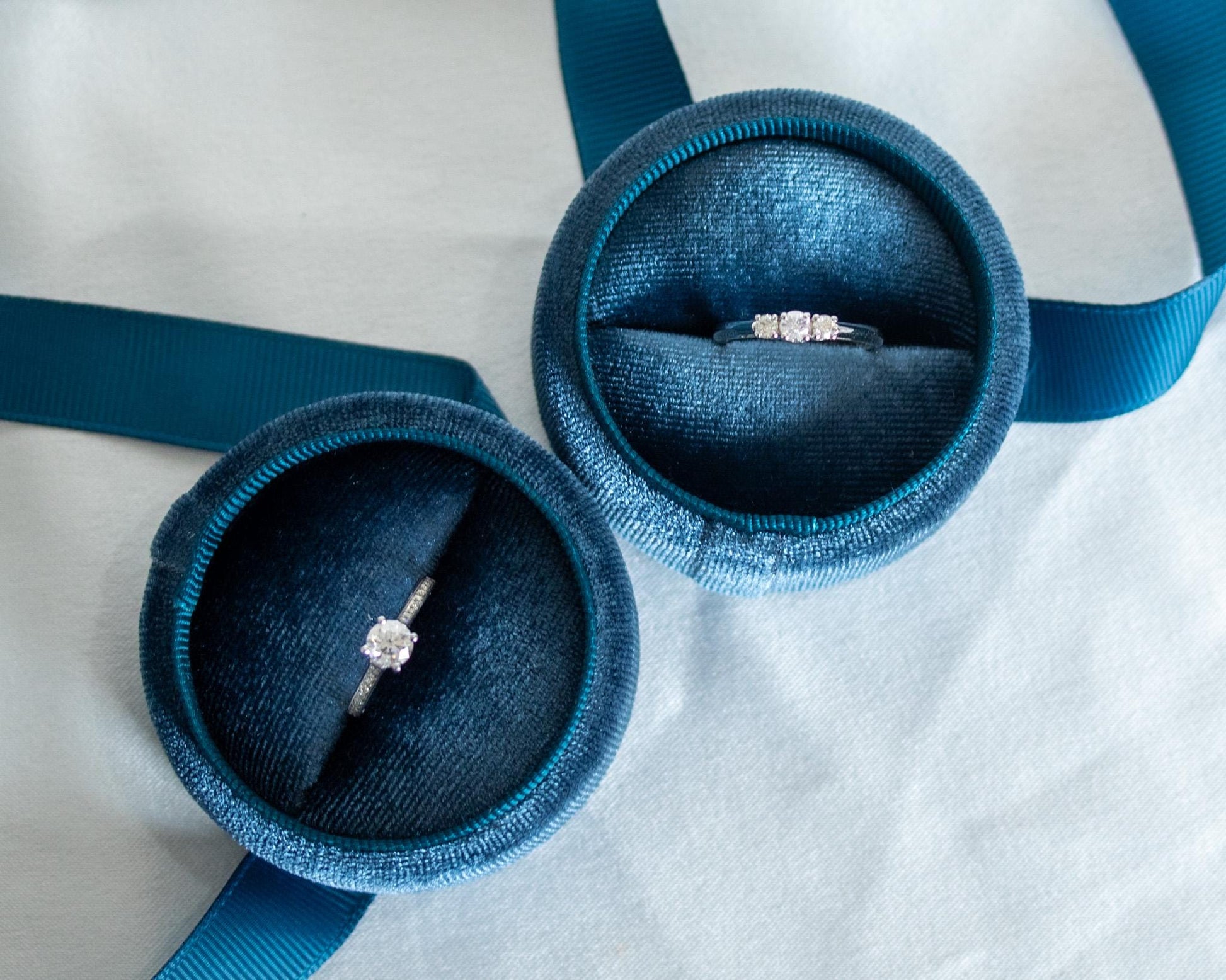 Diamond engagement rings in 14K white gold displayed in blue velvet boxes — one solitaire and one three-stone trilogy design, elegant modern jewelry