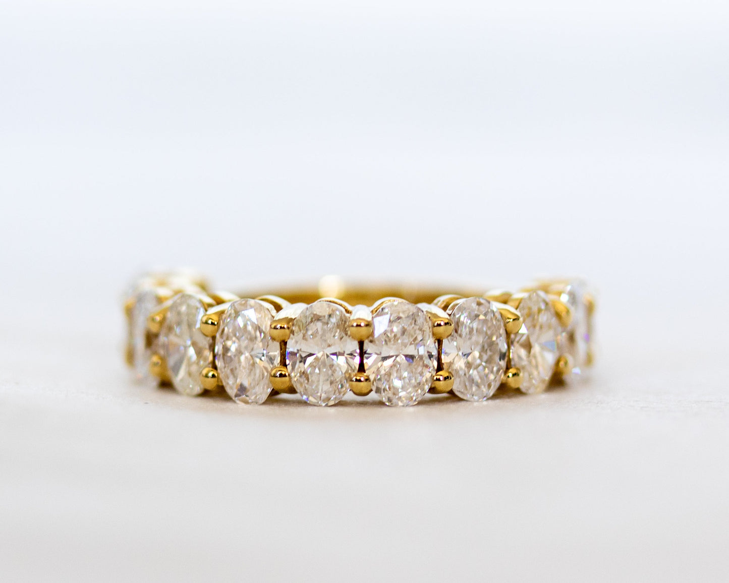 Oval-cut diamond eternity band in polished gold, angled side view