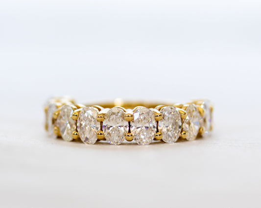 Oval-cut diamond eternity band in polished gold, angled side view