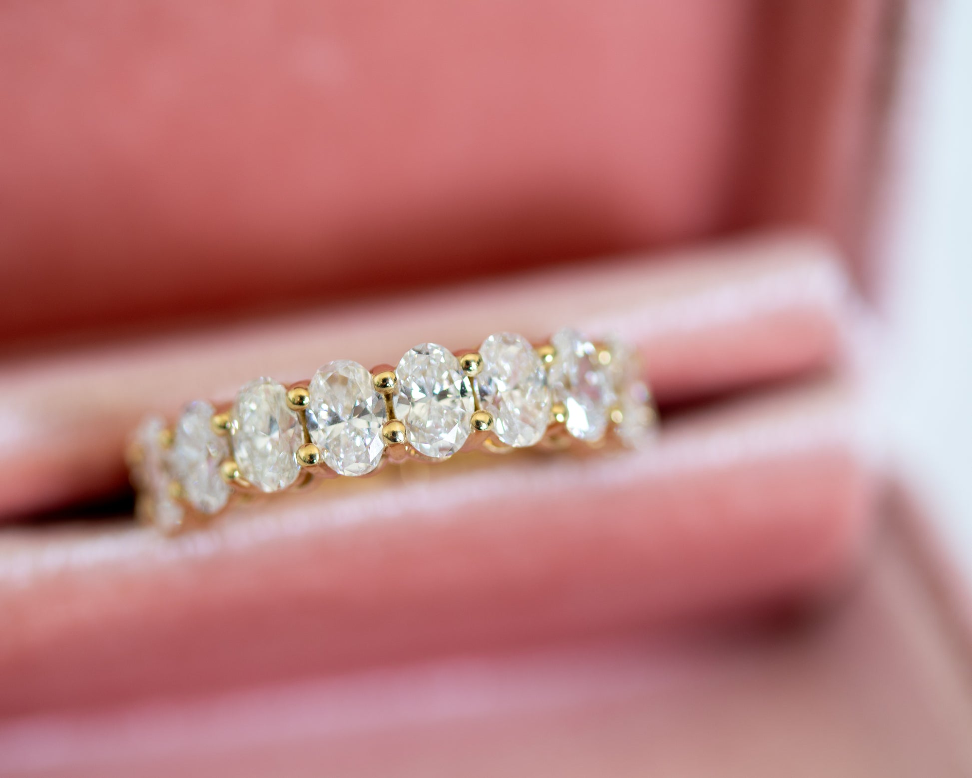 Gold oval-cut diamond eternity band displayed in a blush jewelry box
